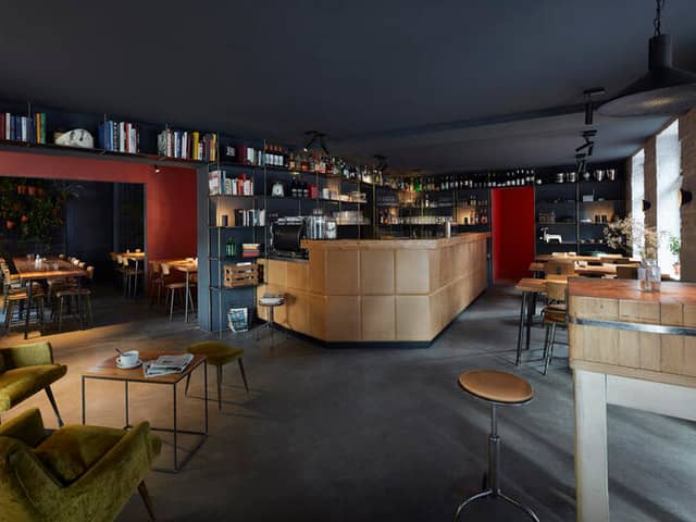 Blick durch den Gastraum auf die helle Holztheke, Bücherregale und den grünen Sessel