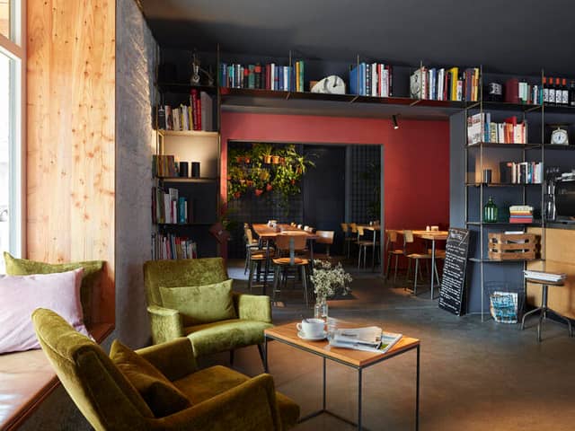 Grüner Retrosessel vor Bücherregalen, daneben ein kleiner Tisch mit Kaffeetasse